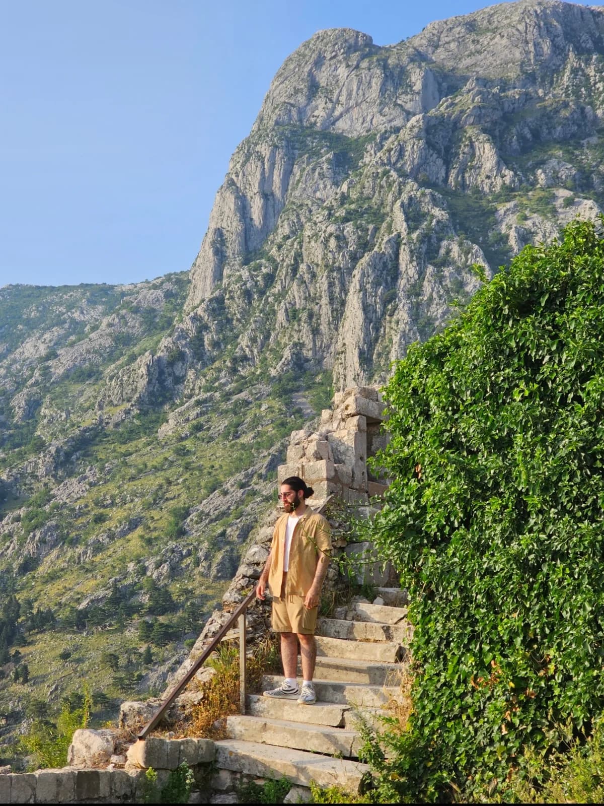 Husaam standing on stone steps with a mountain landscape behind him